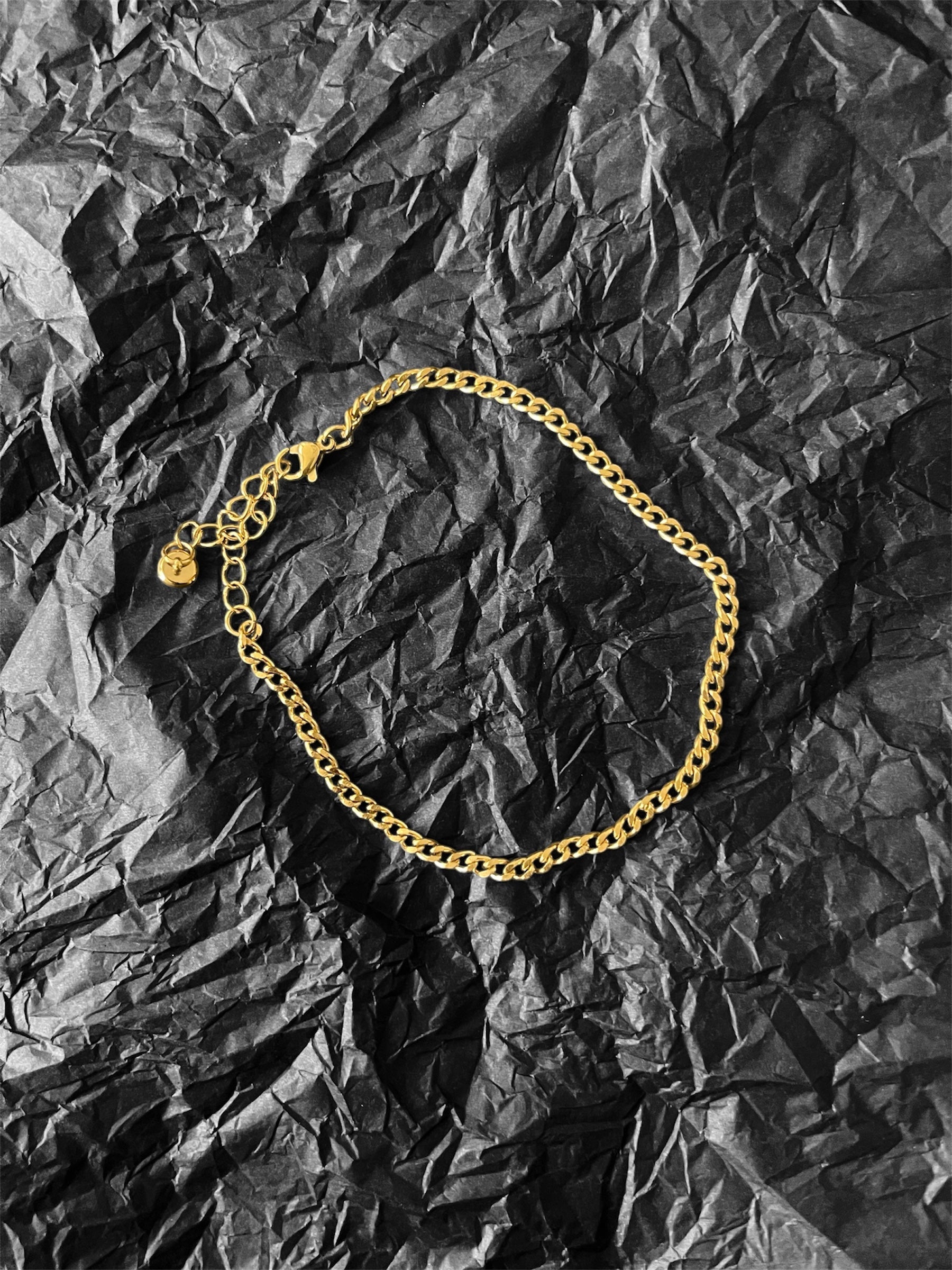 Gold-plated Camille Anklet with adjustable curb chain on black textured background