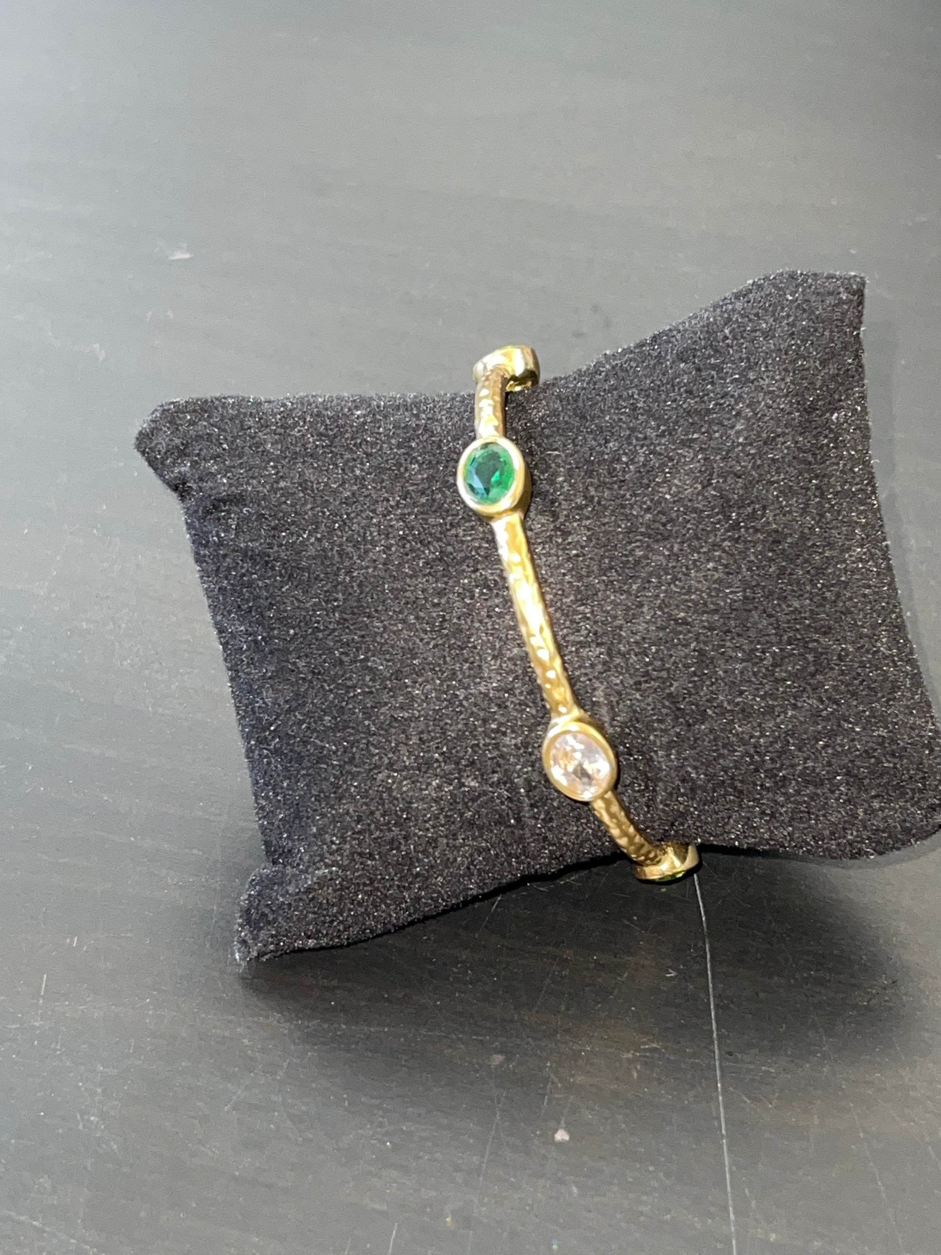 Aurelia Bracelet 18k gold-plated hammered bangle with emerald and clear cubic zirconia stones on black cushion