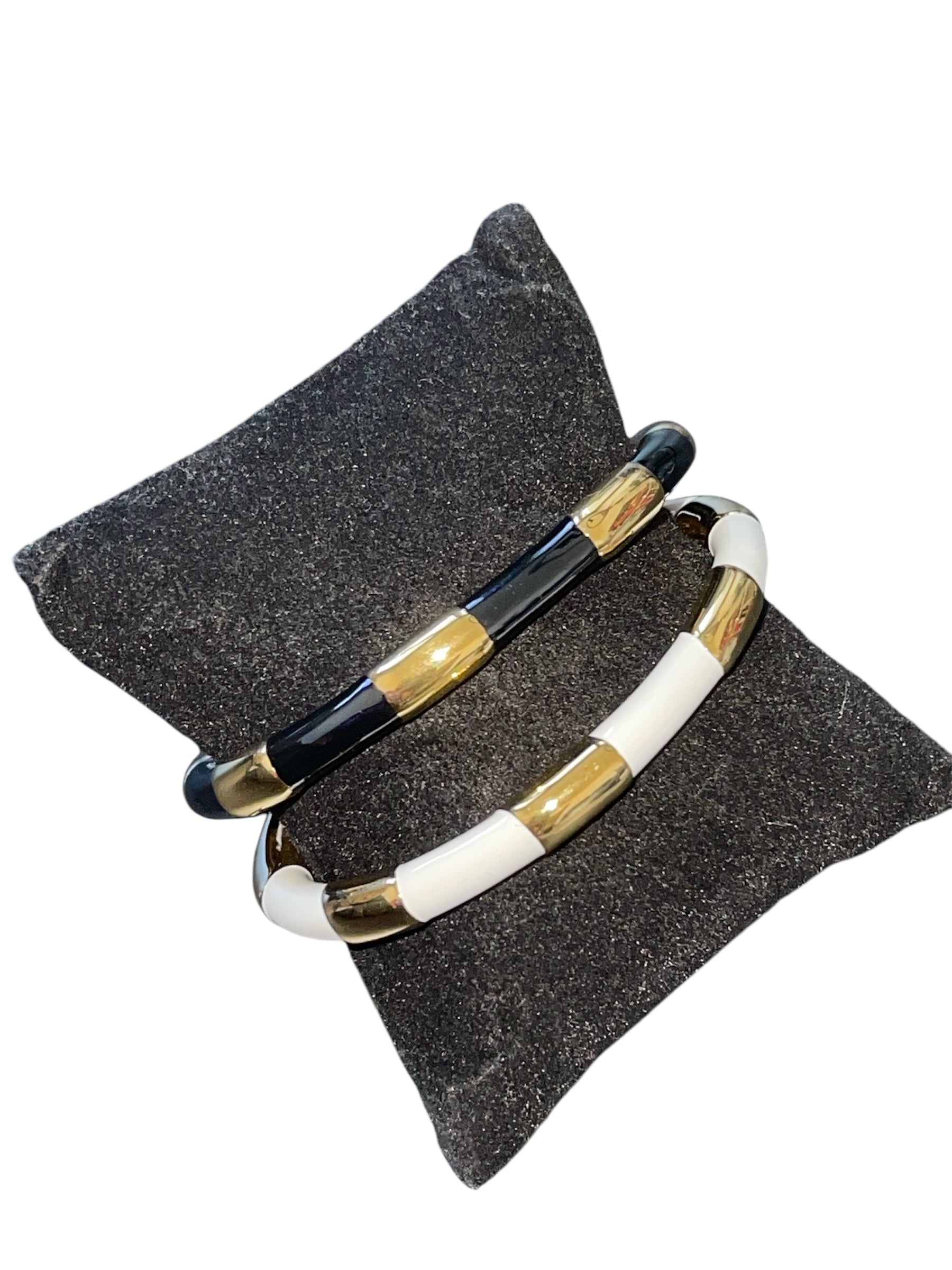 JOANA Bangles in black and white enamel with gold-plated accents on a cushion.