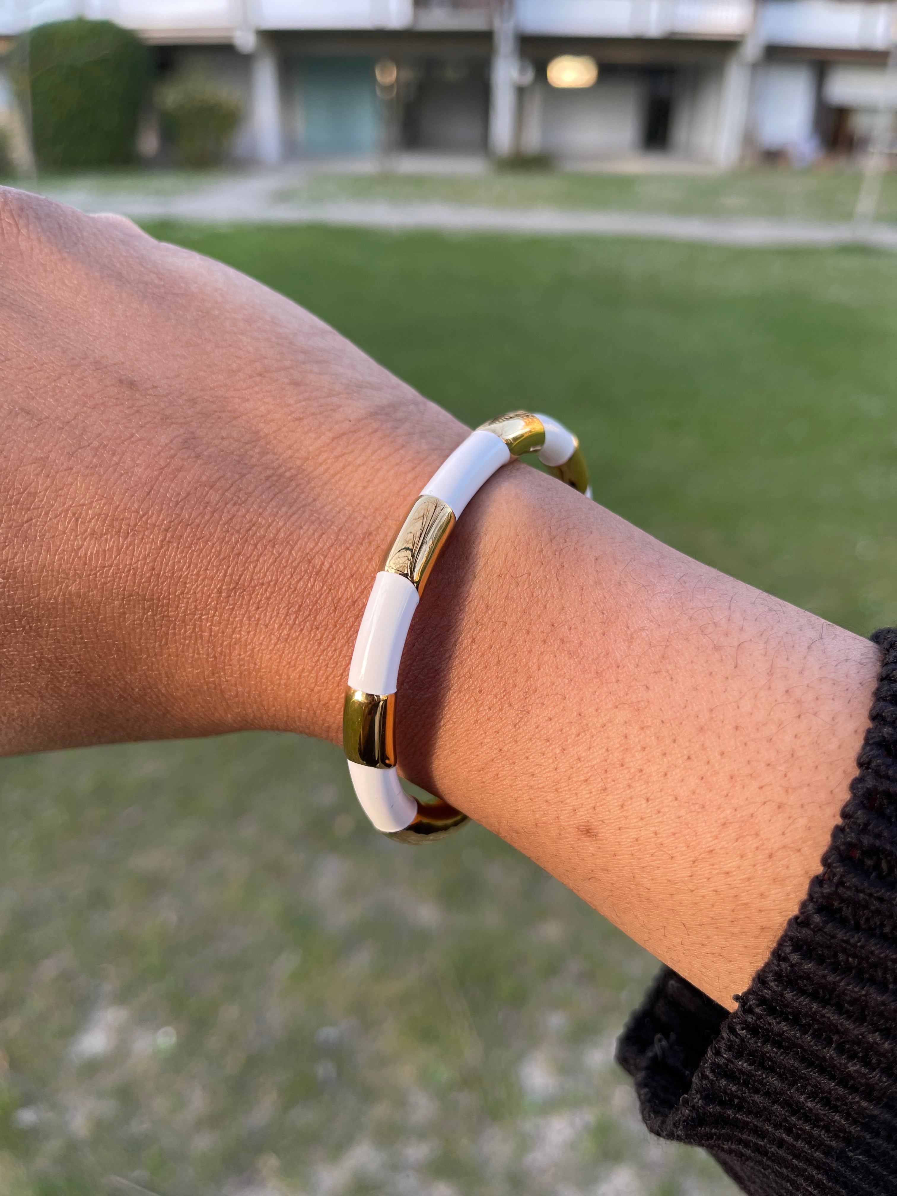 JOANA Bangles with gold-plated accents and white enamel on wrist outdoors.