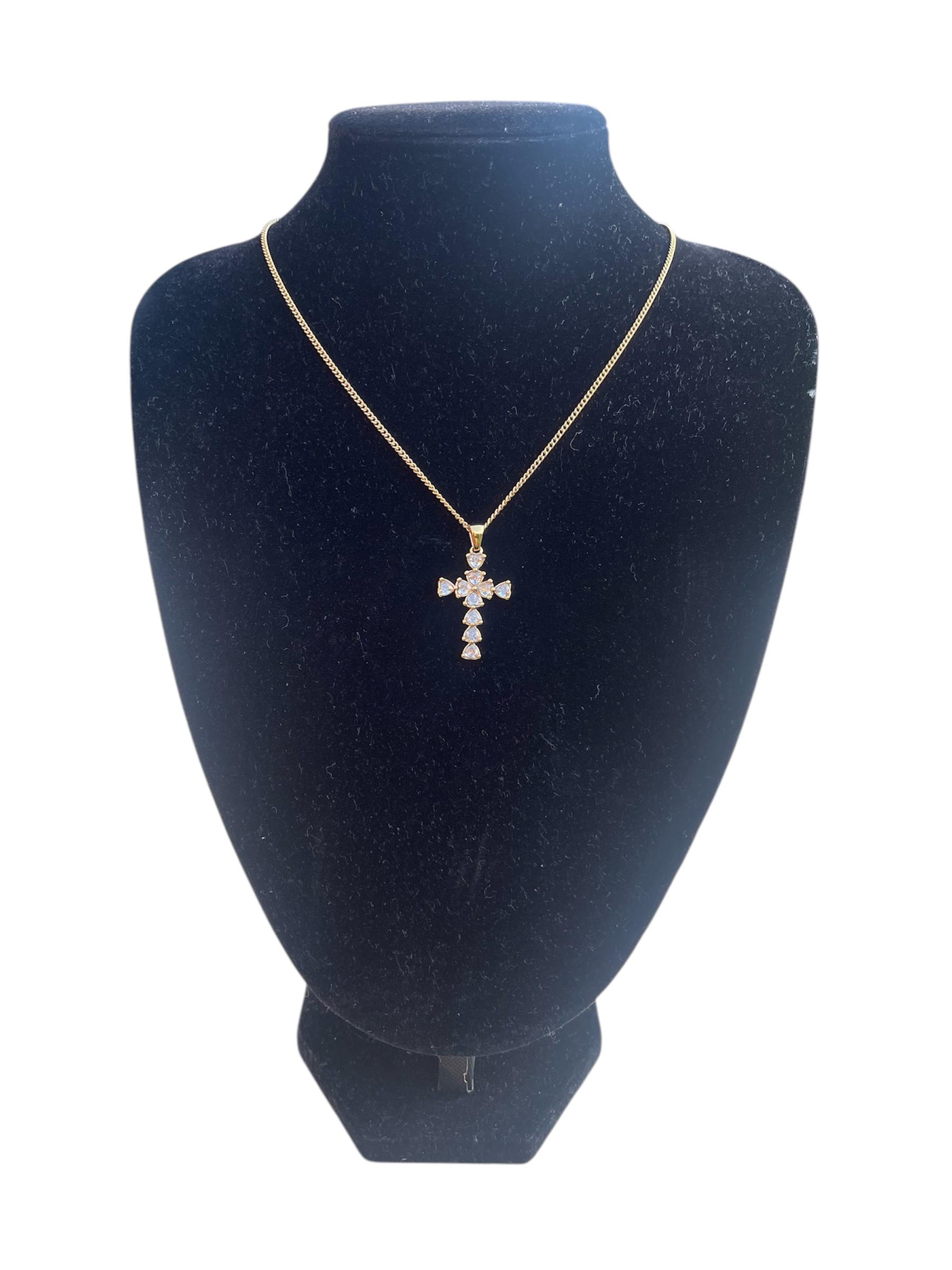 Crystal cross pendant necklace on gold-tone chain displayed on a stand.