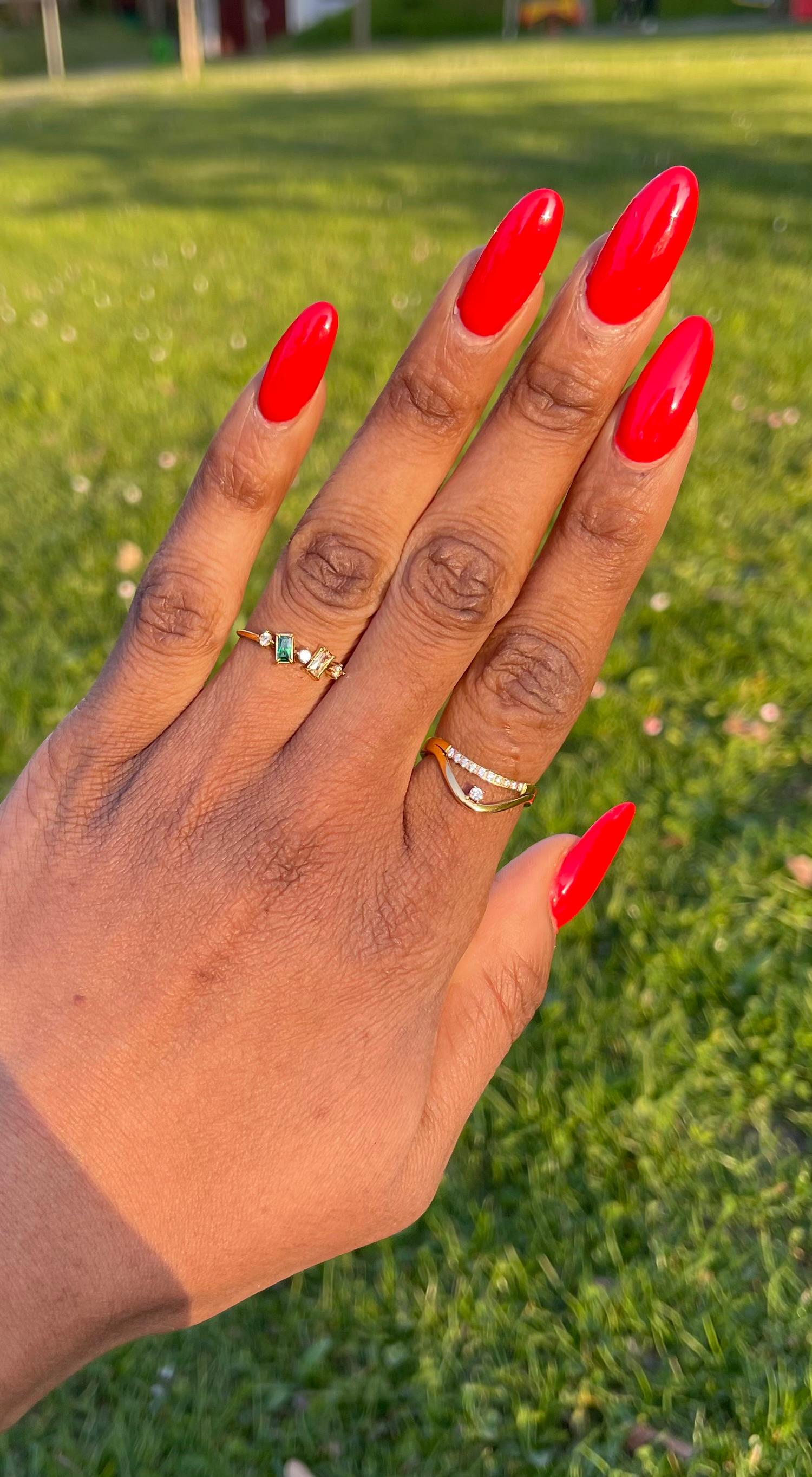 Nina Whisper Ring with baguette-cut stones on hand with red nails, elegant and gold-plated.