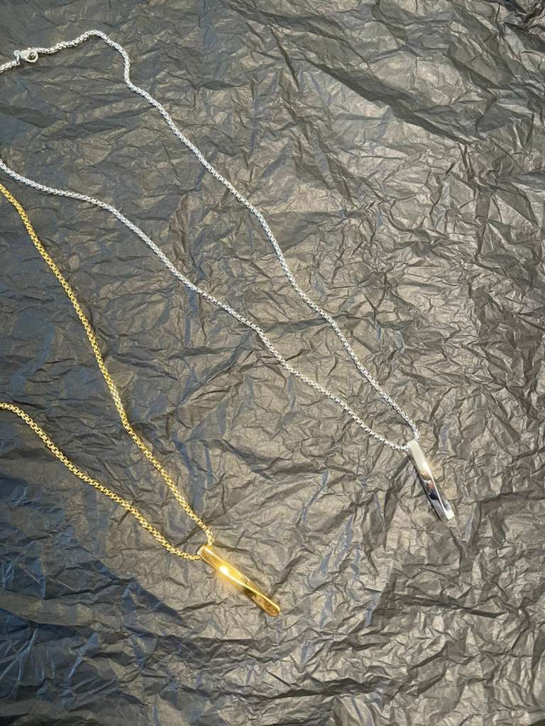 LUCA Necklace minimalist chain with vertical pendant in gold and silver tones on textured black background