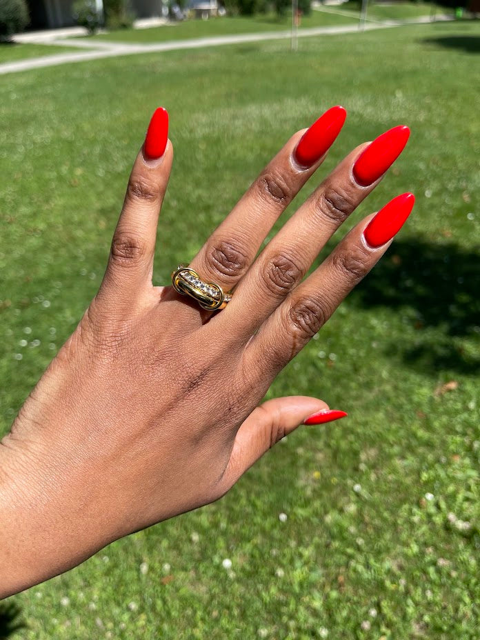 Hand wearing CALISTA Ring with bold 18k gold plating and pavé accents, bright red nails, outdoor background