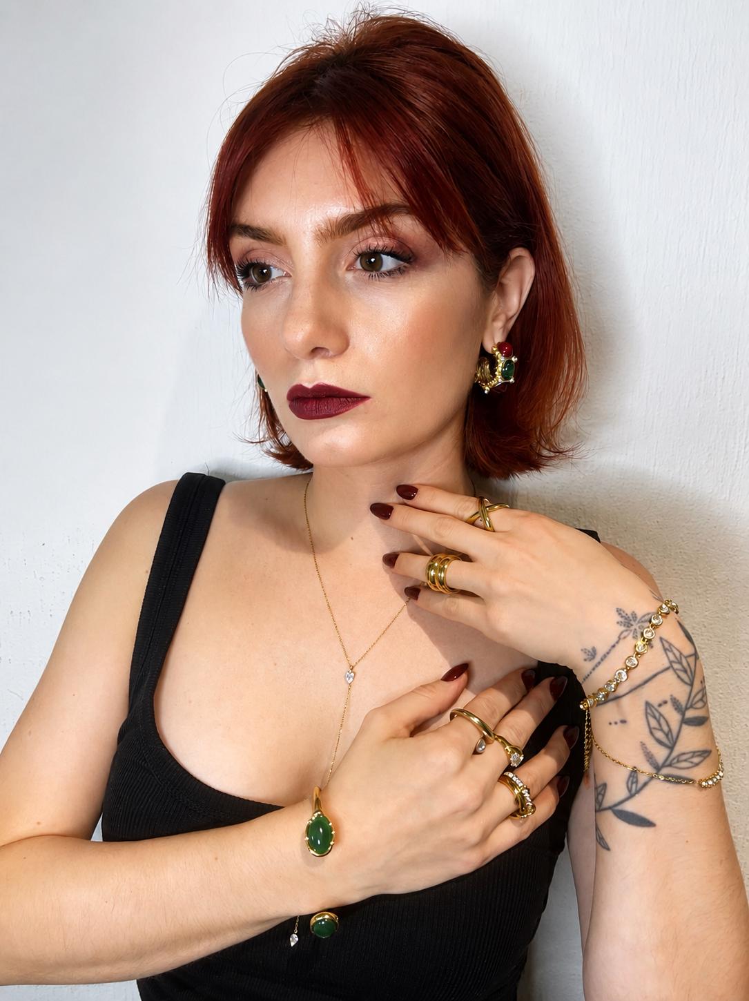 Woman wearing gold jewelry with green gemstones against a white background